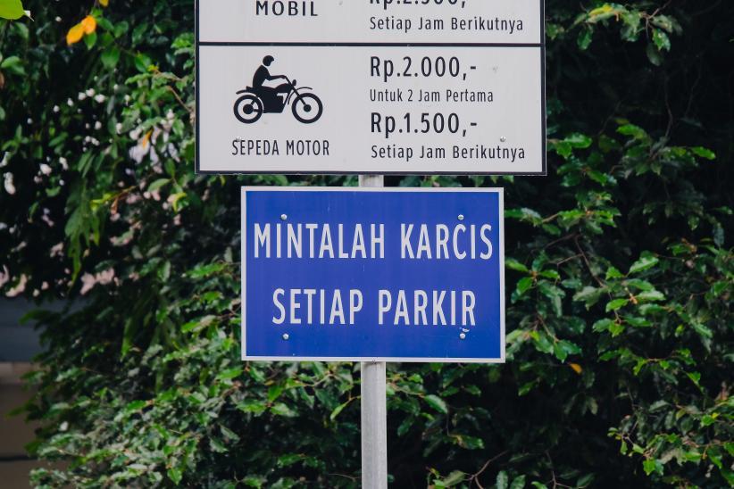 Straatbord in Indonesië met de woorden karcis en parkir, beide afkomstig uit het Nederlands (kaartje en parkeren). Het bord roept op: “Vraag een kaartje (bewijs) bij elke parkeersessie.”
